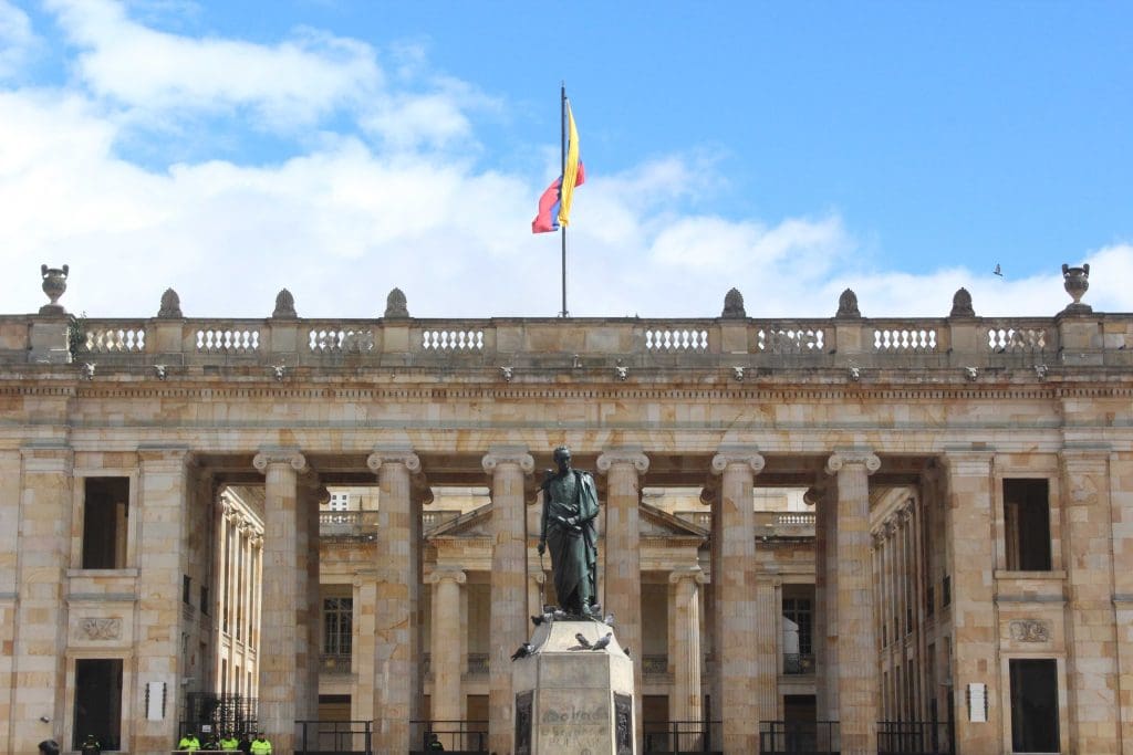 Estátua  na frente de construção clássica na Colombia, com uma bandeira colombiana ao fundo