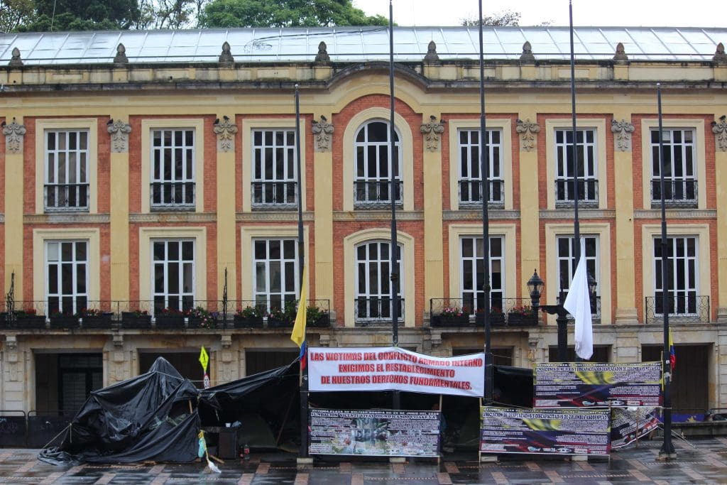 Acampamentp das vítimas do conflito na frente de prédio do governo com banner dizendo " as vítimas do conflito armado interno  exigem o reestabelecimento de nossos direitos fundamentais"