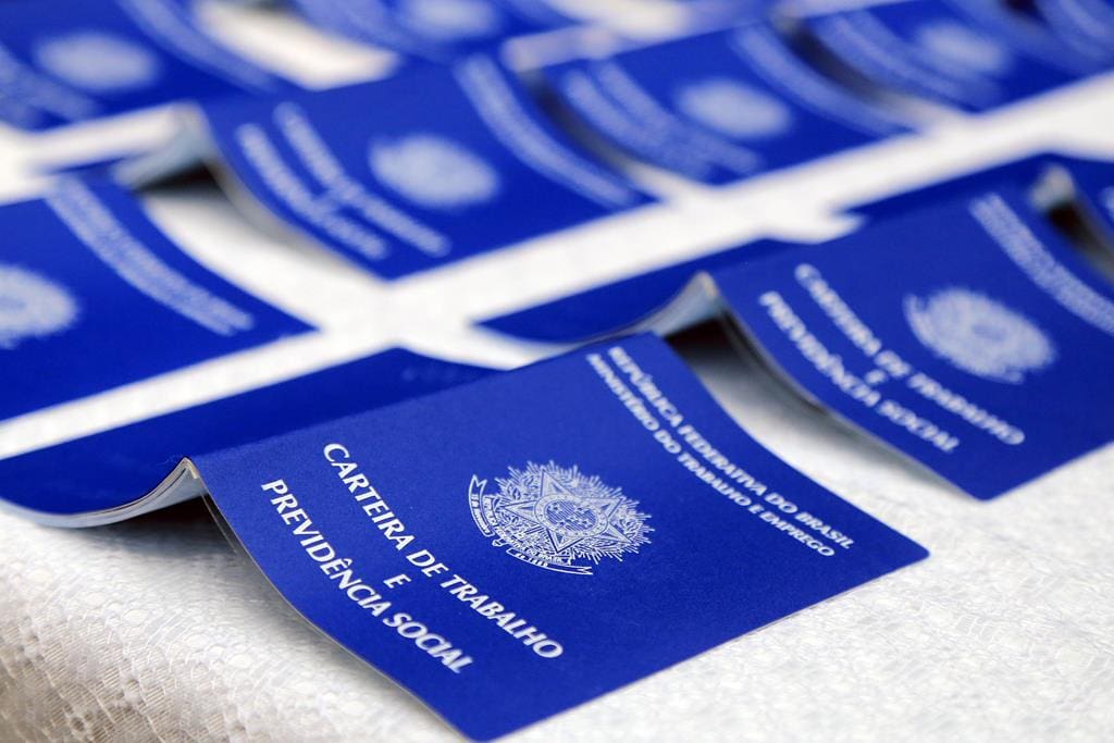 A imagem mostra várias carteiras de trabalho e previdência social disposta em uma mesa. 