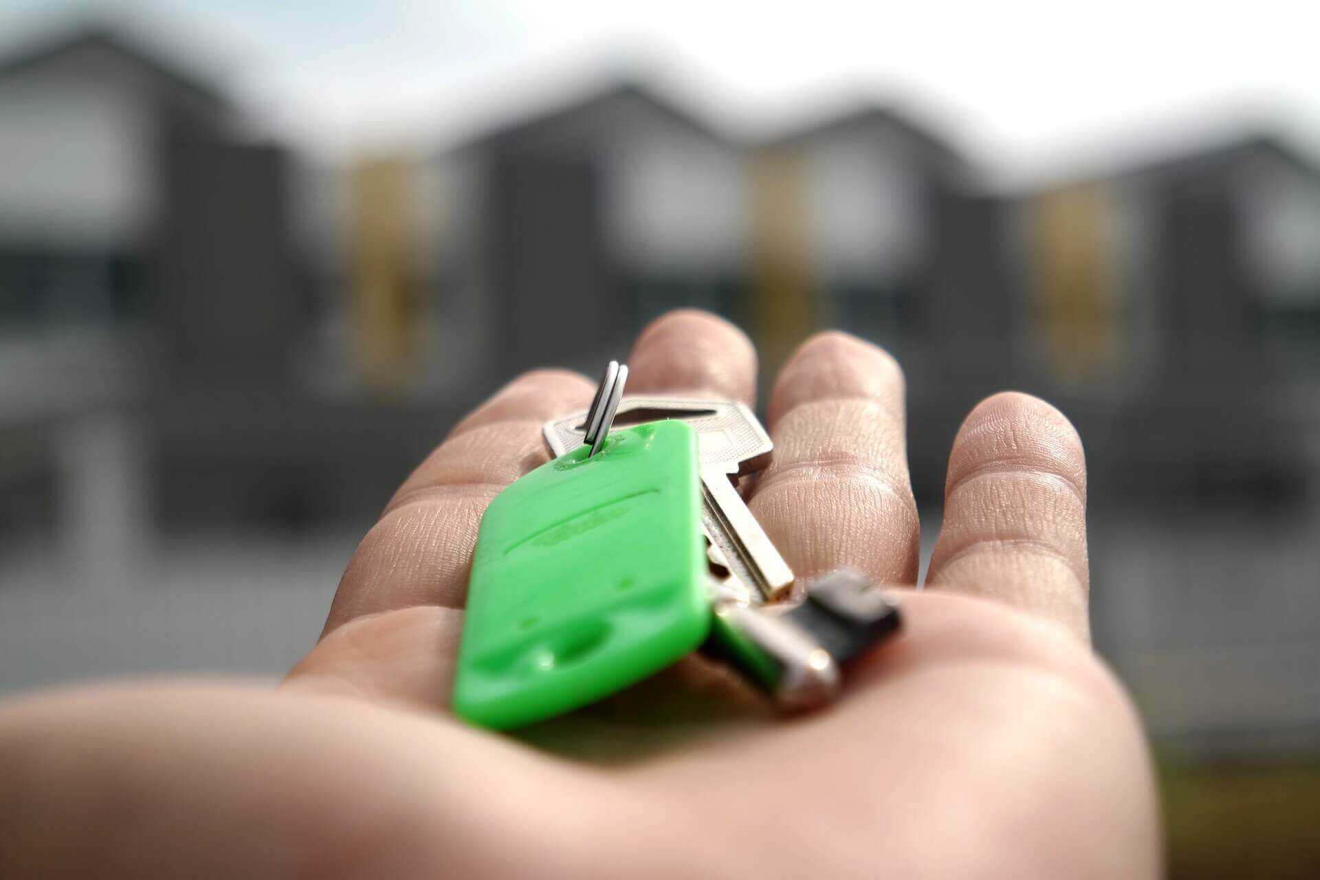 Mão estendida com a chave de um imóvel, além de um chaveiro verde | Direito de propriedade – Artigo Quinto