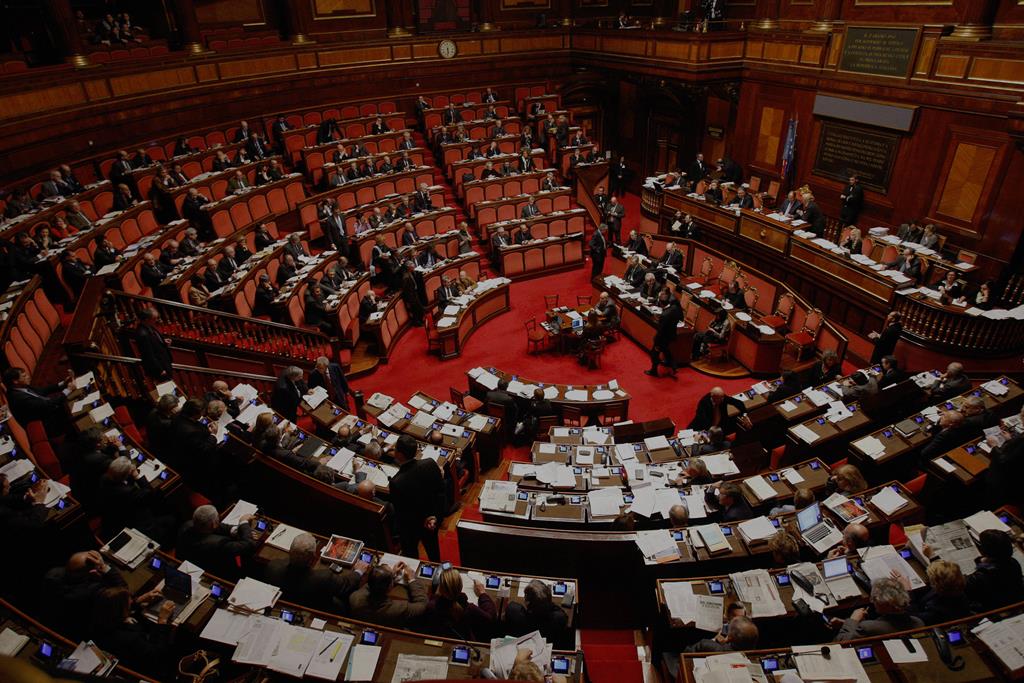 A imagem mostra um exemplo do que é um parlamento. Nele, várias pessoas estão sentadas em bancadas que forma um semicírculo voltado para uma mesa que fica no canto direito.