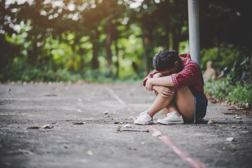 Adolescente sentada no chão com a cabeça apoiada nos joelhos. Texto: O que é abandono afetivo?