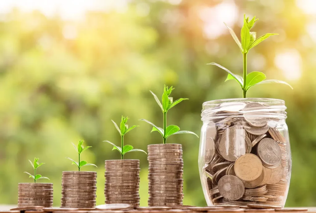 Três pilhas de moeda e um pote de vidro contendo moedas e planta simbolizando aumento do financiamento climático. Texto: COP30: Uma Década do Acordo de Paris e os Desafios do Clima