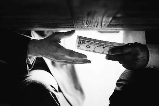 Mãos passando dinheiro debaixo da mesa. Texto sobre fraude no INSS.