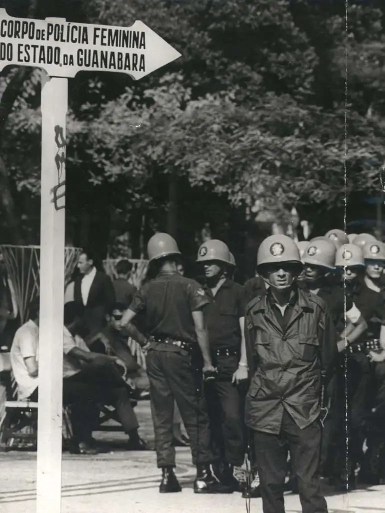 Várias mulheres policiais uniformizadas, em pé, ao lado de uma placa que diz ‘Corpo de Polícia Feminina’. A imagem é um registro histórico da participação feminina na corporação policial do Estado da Guanabara.