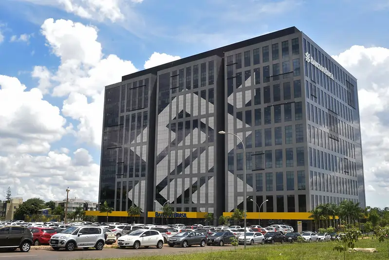 Fachada do Banco do Brasil na Asa Norte, em Brasília – sede de uma das maiores empresas estatais do país, com vidro espelhado e símbolo característico: duas letras “B” entrelaçadas, formando um desenho que lembra um cifrão estilizado.